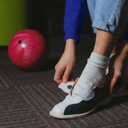 a person putting on bowling shoes next to a bowling ball